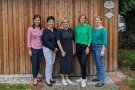 Fünf Frauen stehen vor einer Holzwand